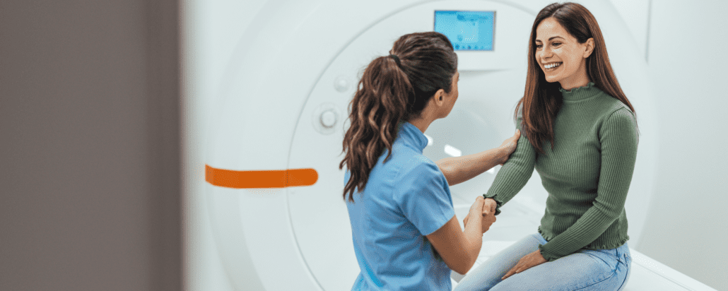 Patient sitting on an exam table speaking with a healthcare provider in front of a medical imaging machine