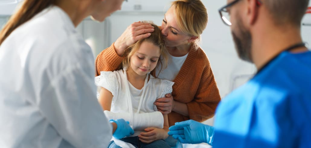 Child receiving medical treatment for an arm injury from healthcare providers in an emergency department setting while caregiver is present